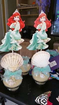 two little mermaids are sitting on top of seashells in glass vases