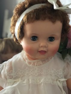 an old doll is wearing a white dress and headband with flowers in the background