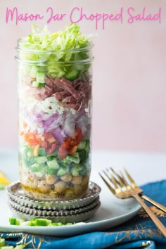 a mason jar filled with chopped salad on top of a plate next to a fork