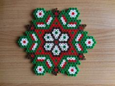 a cross stitch ornament on a wooden surface with red, white and green flowers