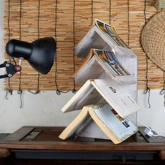 a stack of books sitting on top of a wooden table next to a lamp and wicker wall hanging