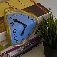 a clock sitting on top of a stack of books next to a potted plant