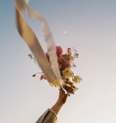 a person holding flowers in their hand with the sky in the background