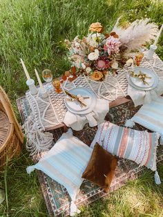 a table set up with place settings and flowers on it in the middle of some grass