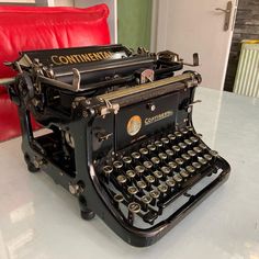 an old fashioned typewriter sitting on top of a table next to a red chair