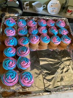 cupcakes with pink and blue frosting are on a baking sheet in the kitchen