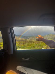 a rainbow appears in the distance as a person holds their hand up to catch it