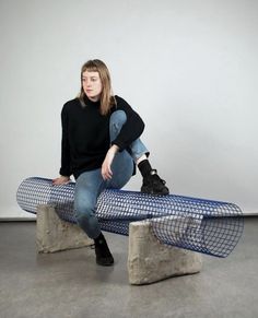 a woman sitting on top of a bench made out of concrete blocks and mesh netting