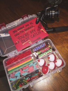 an open plastic box filled with candy and candies next to a fishing rod on a wooden table