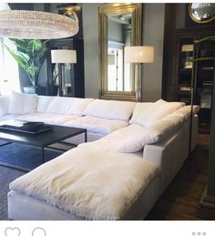 a large white sectional couch sitting in a living room next to a table with a lamp on it