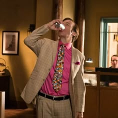 a man in a suit and tie drinking from a cup while another man looks on