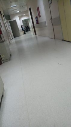 an empty hospital hallway with white floors and yellow doors on either side of the room