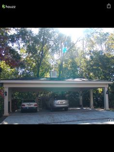 two cars are parked in the driveway under a covered carport with trees behind them