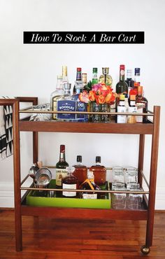 a bar cart with liquor bottles and glasses on the top, labeled how to stock a bar cart