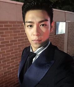 a man in a suit and tie standing next to a brick wall