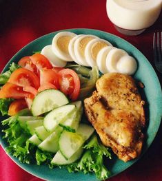 a blue plate topped with chicken, cucumbers and tomatoes next to a glass of milk