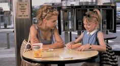 a woman and child sitting at a table with food in front of them on the sidewalk