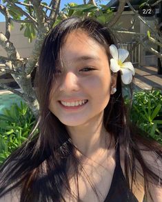 a woman with long hair and a flower in her hair smiling at the camera while wearing a black tank top