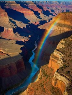 a rainbow shines brightly in the sky above a canyon and river below it,