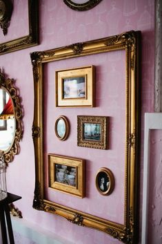 a pink wall with gold framed pictures on the wall and a mirror hanging above it