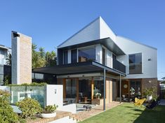 a modern house with an outdoor patio and lawn area in the foreground on a sunny day