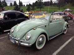 an old green car parked in a parking lot next to other antique cars and people