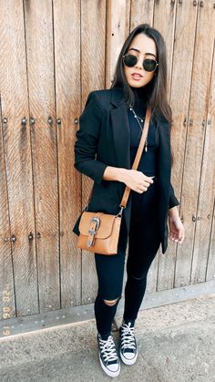 a woman in black jacket and sunglasses holding a brown purse