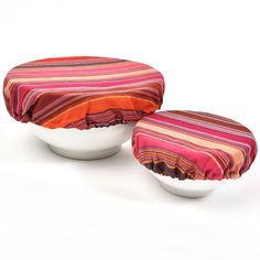 two white bowls with red and orange striped covers sitting on top of each other in front of a white background