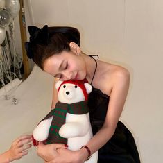 a woman holding a white teddy bear in her arms while wearing a red and green scarf