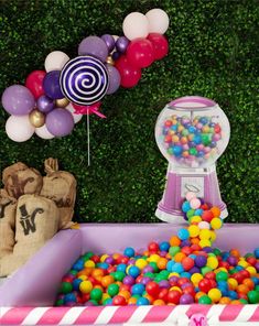 there is a pink ball pit with many balls in it and balloons on the wall