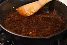 a wooden spoon in a pan on top of a stove with food cooking over it