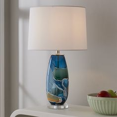 a lamp that is on top of a table next to a bowl with an apple in it