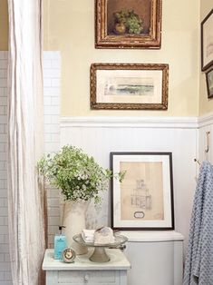 a white toilet sitting in a bathroom next to a painting and pictures on the wall