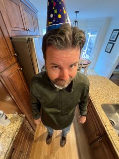 a man with a party hat on his head standing in the middle of a kitchen