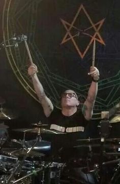 a man is playing drums in front of a pentagramus symbol on the wall