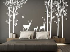 a bed sitting under a white tree wall decal next to a night stand with two deer on it