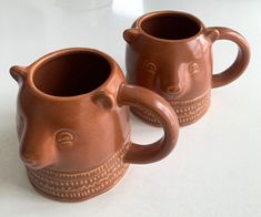 two brown mugs sitting on top of a white table next to each other with faces drawn on them