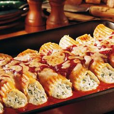 a pan filled with ravioli covered in sauce on top of a wooden table next to bread