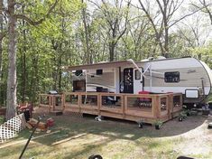 an rv is parked in the woods next to a deck and picnic table with chairs