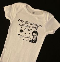 "A funny designed Onesies® features the phrase \"Grandpa Loves Me And Elvis\". Nothing matters more than a baby's comfort, and this one piece is the right choice for all active babies. The envelope neckline and three snap leg closure ensure comfort throughout the day. This is a perfect gift for Mom, Grandma, Baby Shower Gift or just because for that Little One! These gender neutral Gerber brand Onesies® are incredibly comfy! Both the bodysuits and t-shirts are printed on 100% cotton for a super Funny Customizable Fitted Onesie, Funny Customizable Short Sleeve Onesie, Funny Short Sleeve Onesie With Name Print, Funny Short Sleeve Bodysuit With Letter Print, Funny Short Sleeve Letter Print Bodysuit, Unisex Cute Onesie With Graphic Print, Funny Graphic Print Onesie, Father's Day Cotton Onesie With Graphic Print, Funny Unisex Onesie With Letter Print