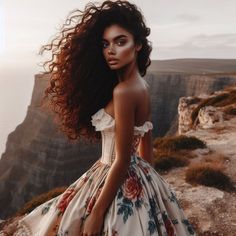 a woman with long hair standing on top of a cliff looking at the camera while wearing a floral dress