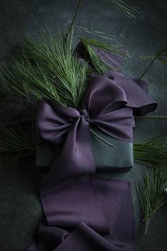 a present wrapped in purple paper and tied with a green ribbon next to pine branches