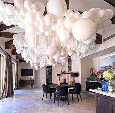 a room filled with lots of white balloons hanging from the ceiling and tables covered in black chairs