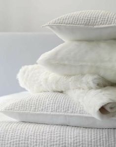 three pillows stacked on top of each other with white sheets and pillow cases in the background