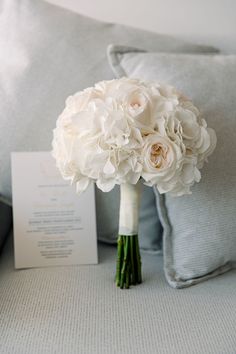 a bouquet of white flowers sitting on top of a bed next to a card and pillow