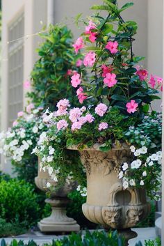 pink and white flowers are in large urns on the side of a building with greenery