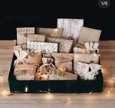 there are many wrapped presents in the box with lights around them and on the table