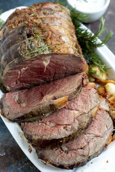 sliced roast beef on a platter with potatoes and herbs