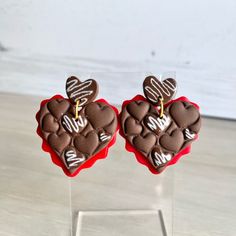 two heart shaped cookies with chocolate frosting on them sitting in front of a clear acrylic stand