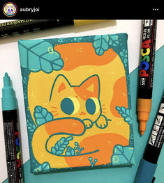 an orange cat is sitting on top of a blue notebook and some markers are next to it